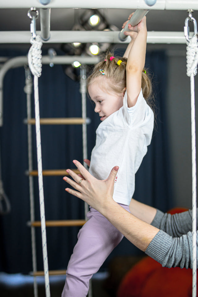 Parent supporting a young girl as she climbs an indoor play gym, an example of controlled risky play