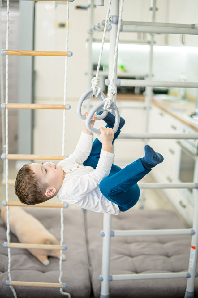 Child hanging on gymnastic rings on a Brainrich home play gym with crash mats below
