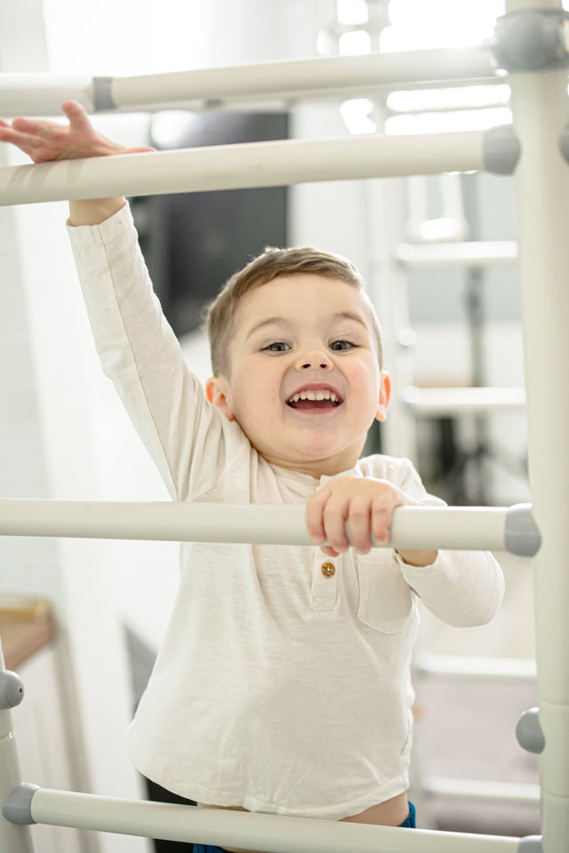 Smiling toddler climbing a white steel home sensory gym