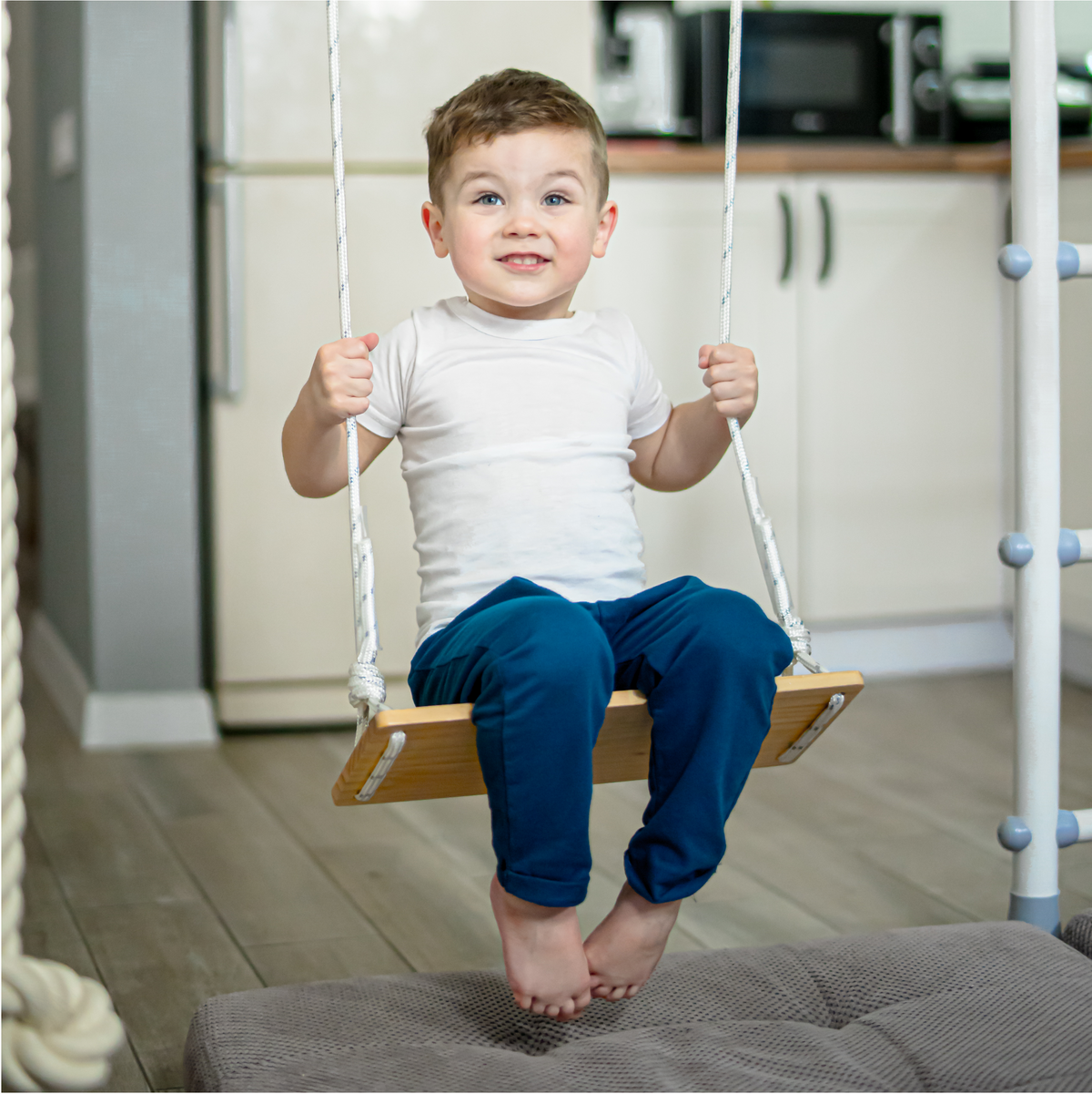 Boy on a wooden swing hung inside a Brainrich indoor play gym frame