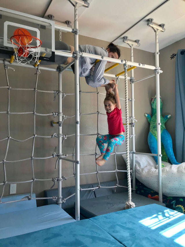 Dad supporting his daughter as she hangs from an overhead bar on a Brainrich home play gym