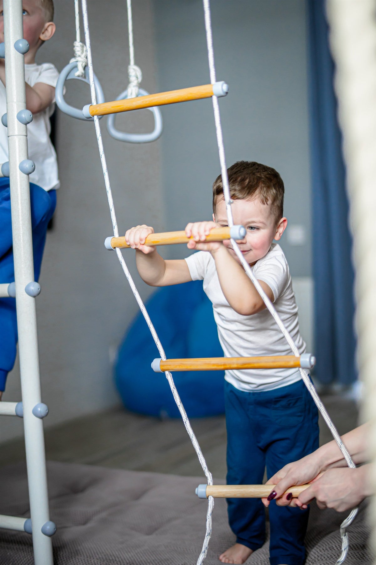 Boy climbing the rope ladder of a Brainrich play gym set up in a basement playroom