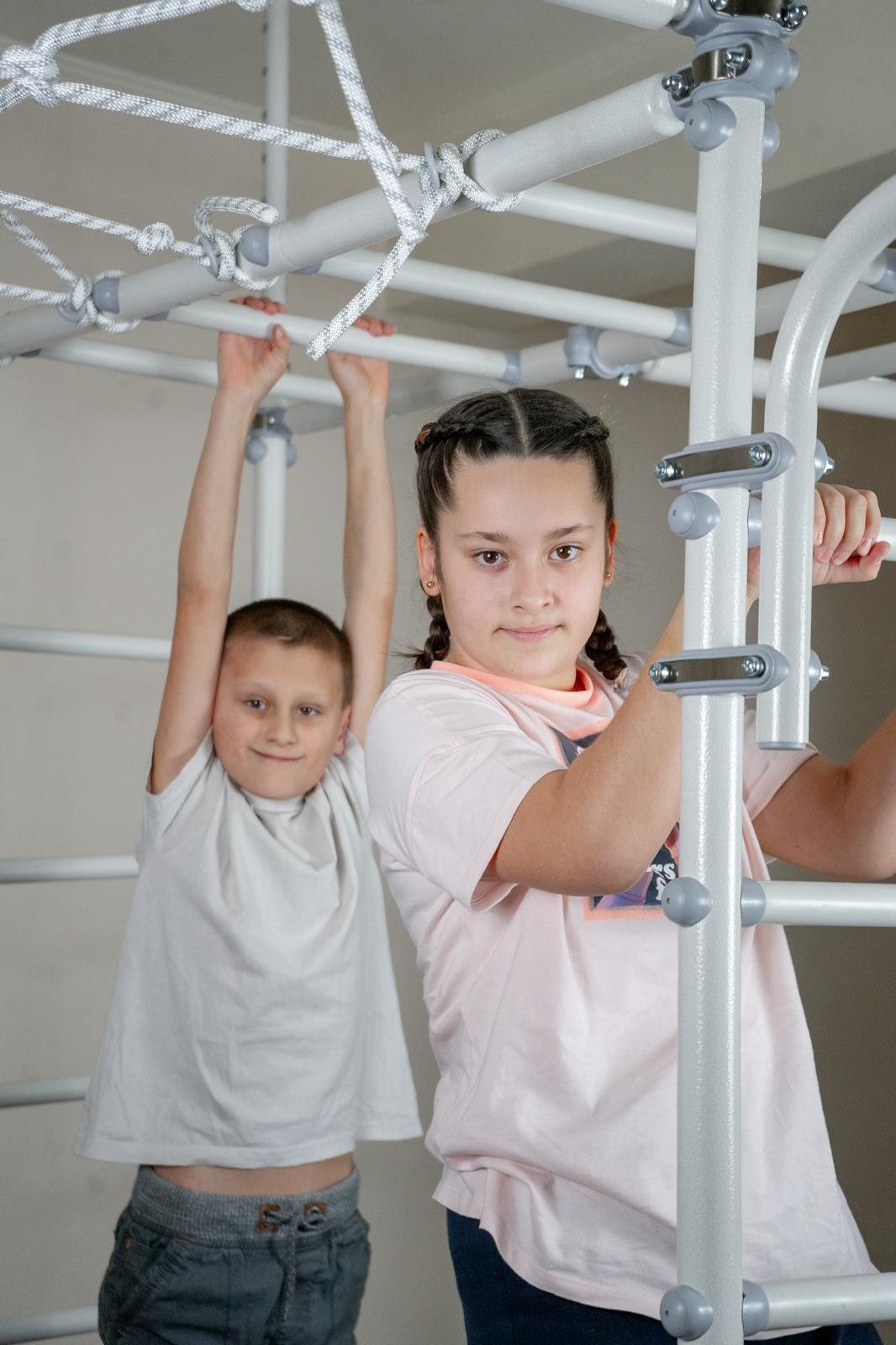 A sister and brother hang from the bars of a Brainrich indoor gym