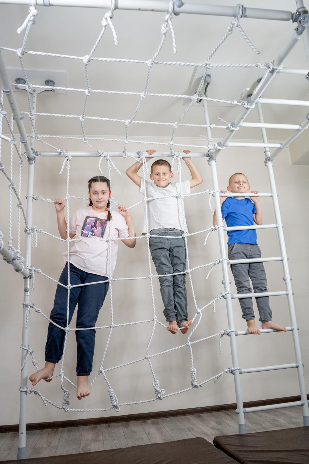 Three kids climbing the net of a Brainrich Mega Max indoor play gym