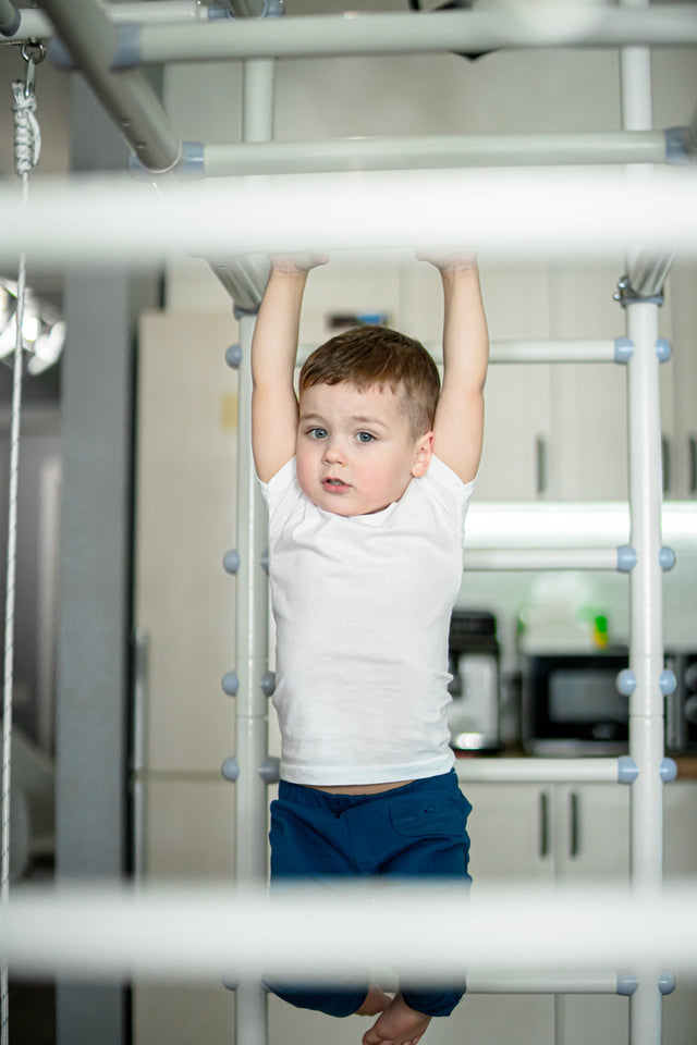 Toddler hanging from the top bar of a Brainrich play gym with a parent close by