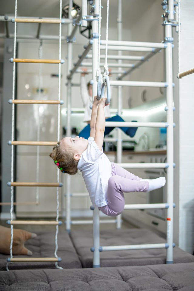 Young girl calmly reaching for gymnastics rings on a Brainrich home play gym, a sensory movement break in an autism homeschool