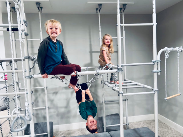 A family with a toddler at their Brainrich home play gym in a family room, the kind of PE equipment homeschool funding programs can cover