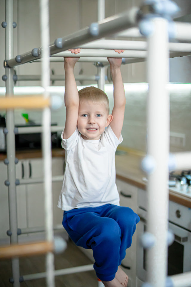 Boy hanging from the monkey bars of a Brainrich home play gym in the kitchen, movement woven into the school day
