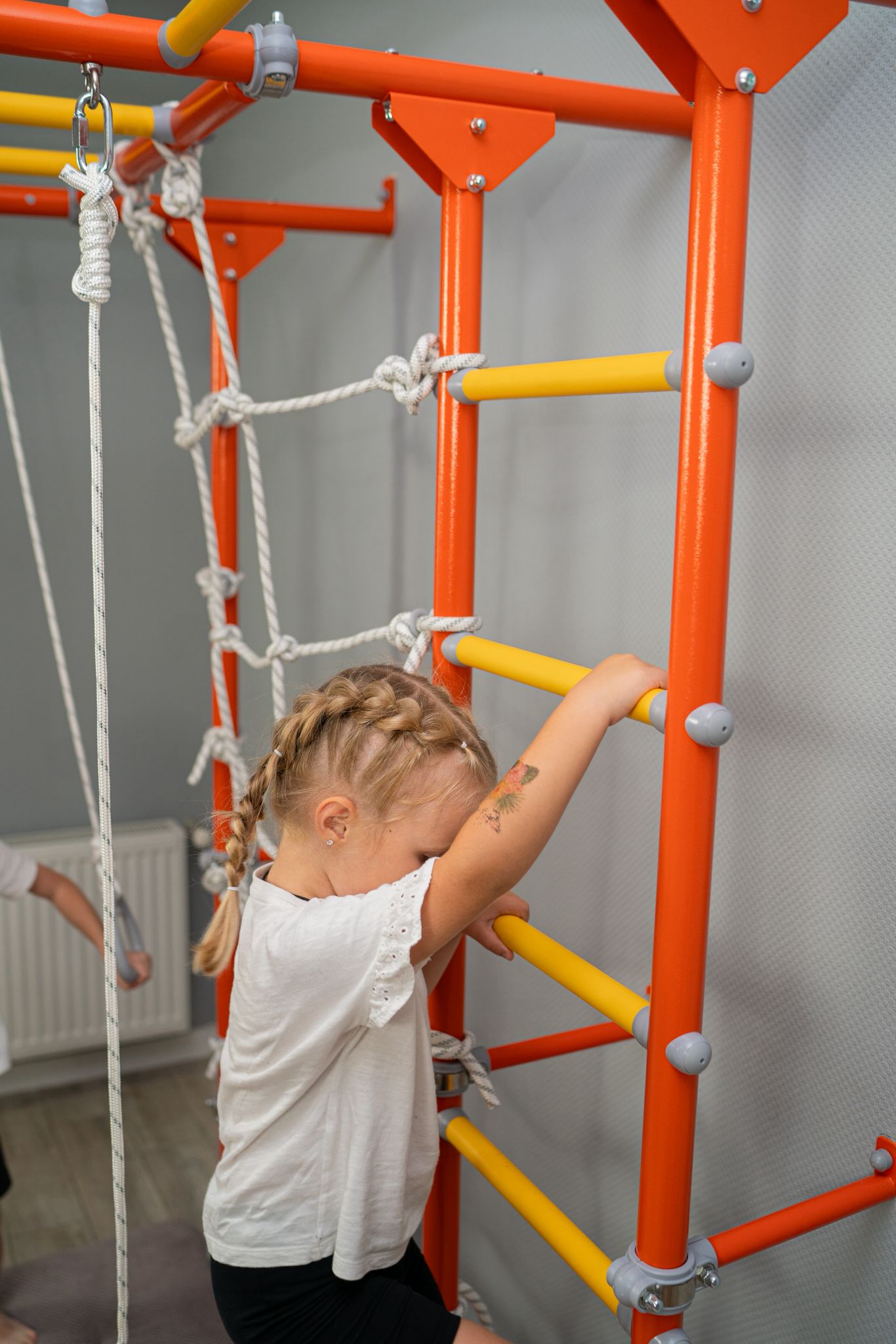Young girl calmly climbing the ladder of a Brainrich home play gym in a quiet grey room
