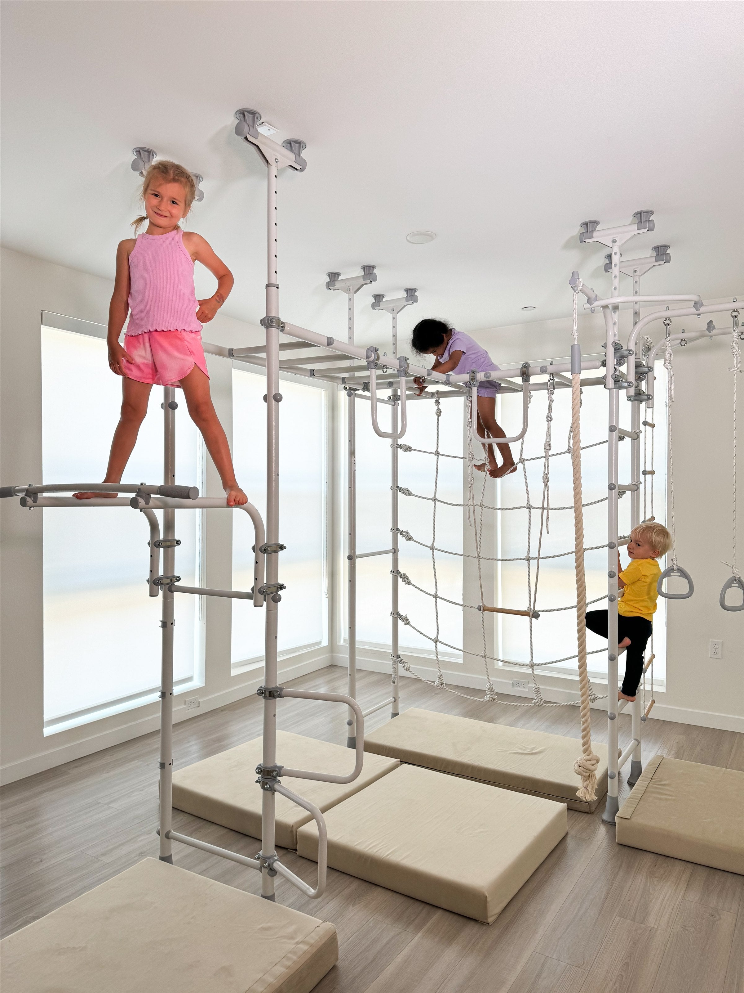 Three kids climbing on a white Brainrich indoor play gym in a bright room, the indoor movement zone that carries a year-round homeschool schedule through every season