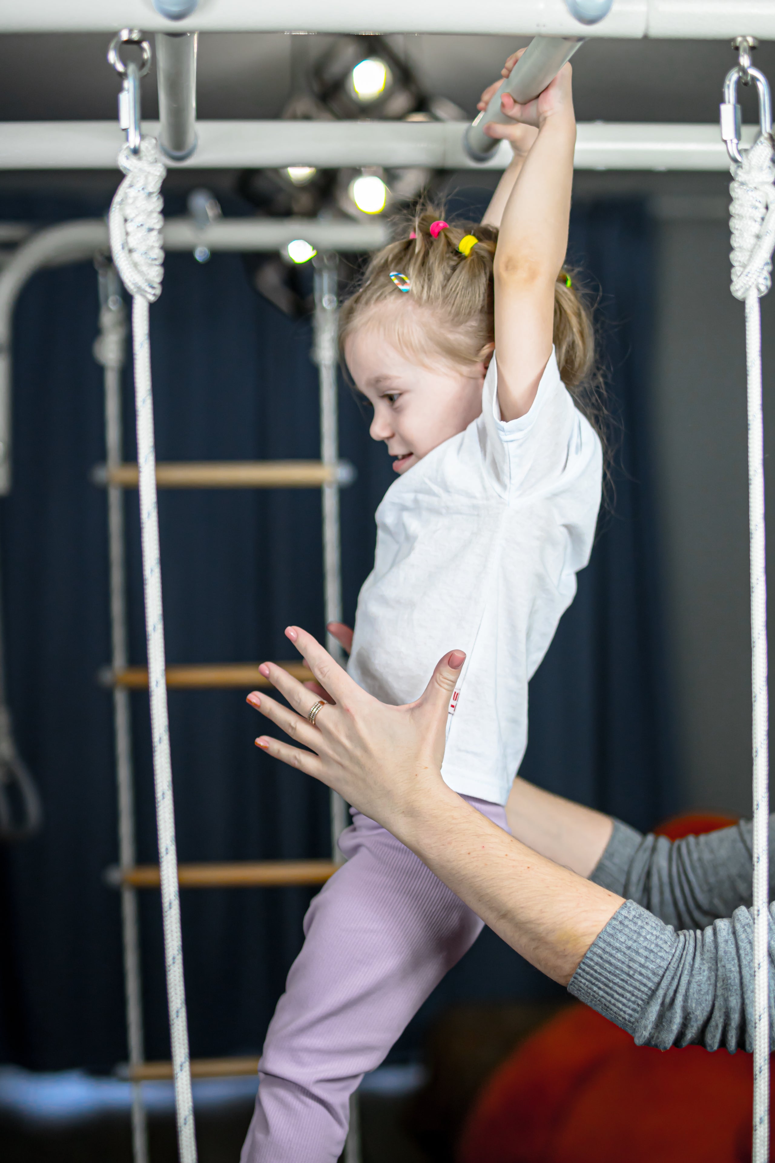 Parent supporting a young girl as she climbs an indoor play gym, an example of controlled risky play