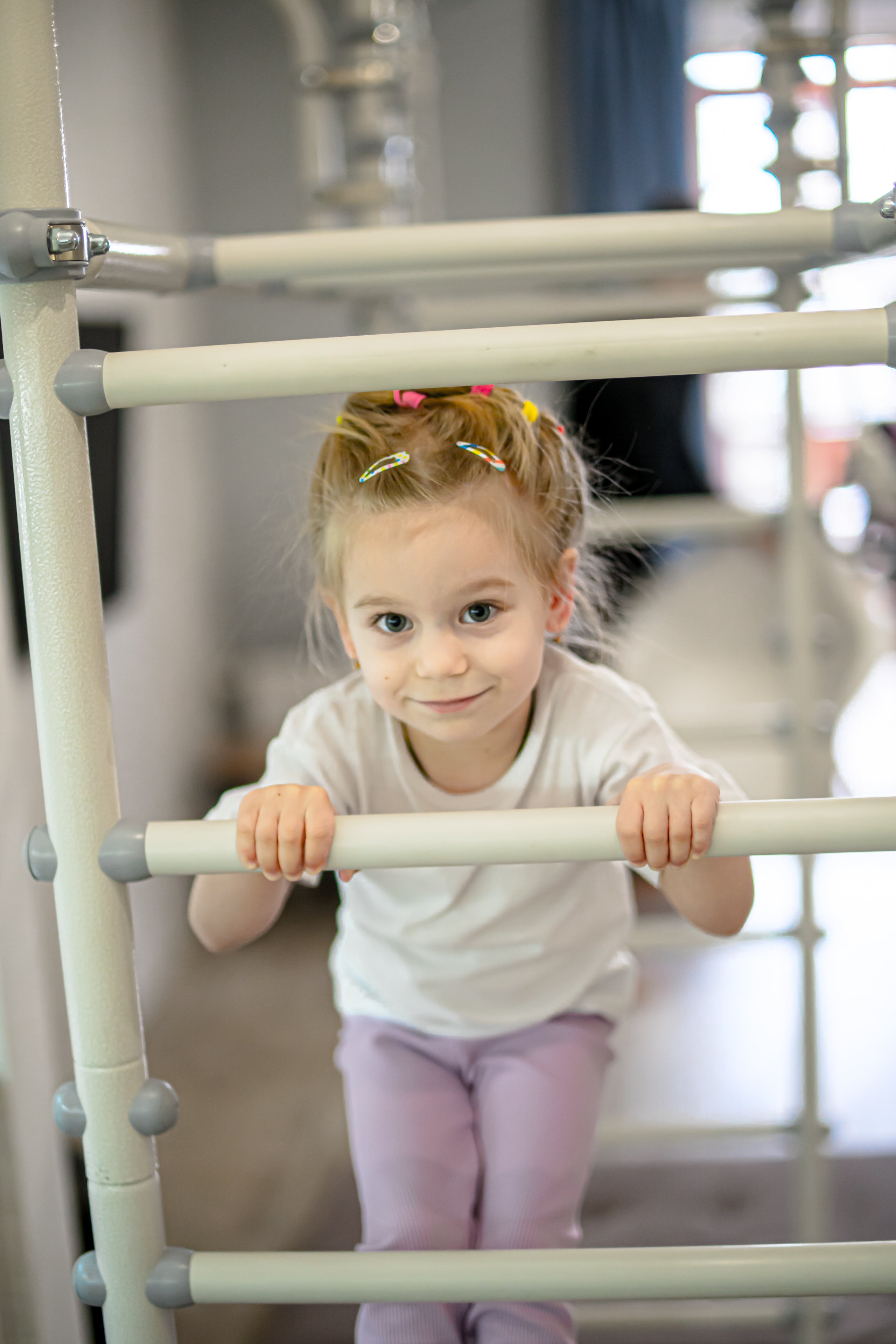 Young girl gripping the rungs of a steel play gym, a classic heavy work activity for kids