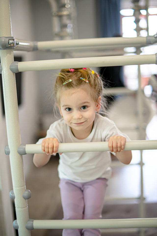 Young girl gripping the rungs of a steel play gym, a classic heavy work activity for kids