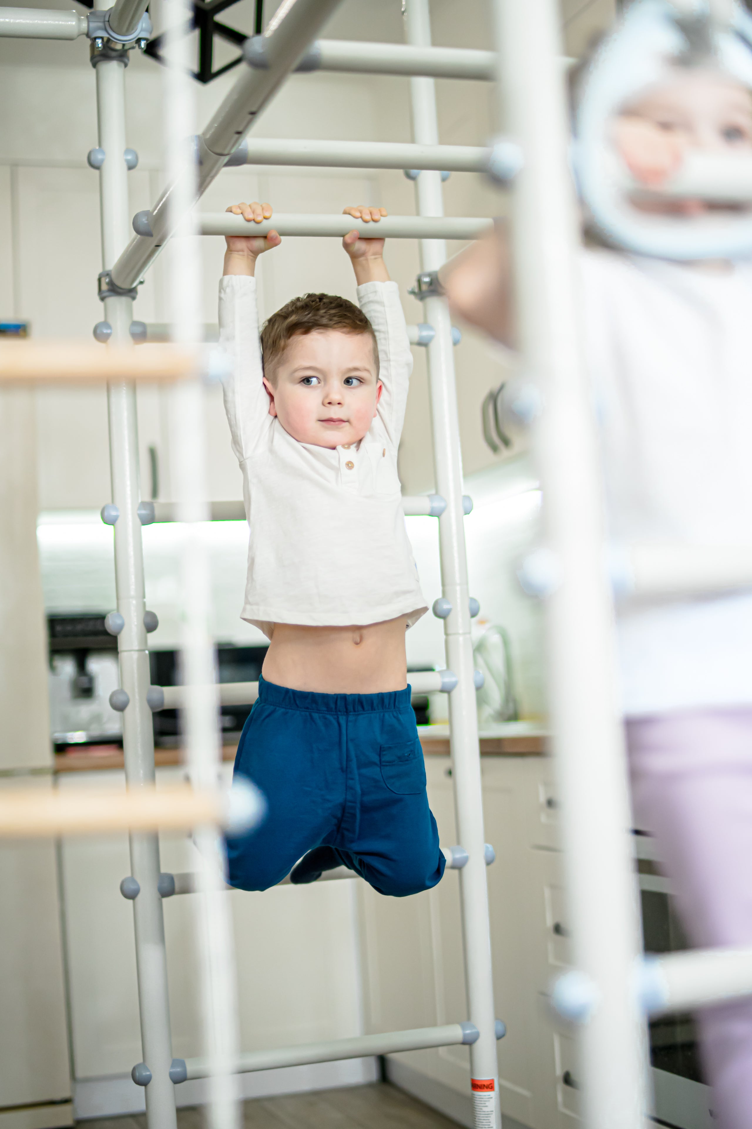 Boy getting daily sensory input hanging from an indoor play gym bar at home