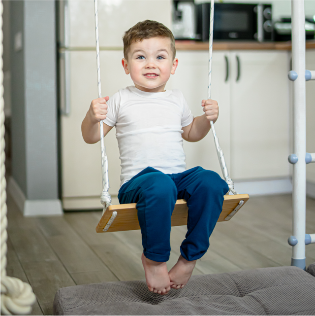 Boy on a wooden swing hung inside a Brainrich indoor play gym frame
