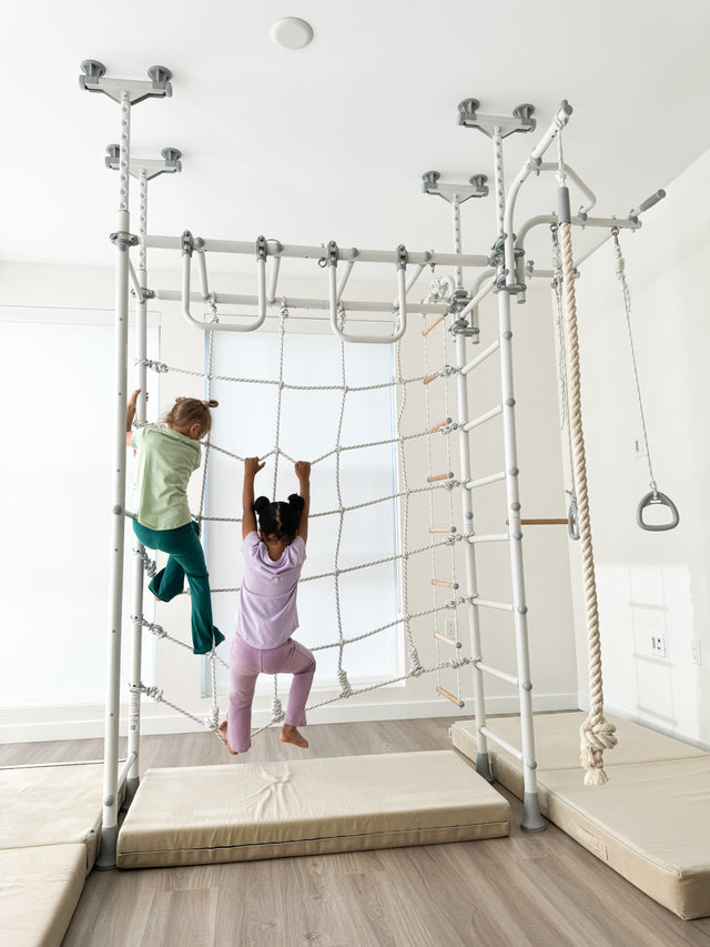 Two girls climbing the rope net of a Brainrich steel play gym, a safe redirect for furniture climbing