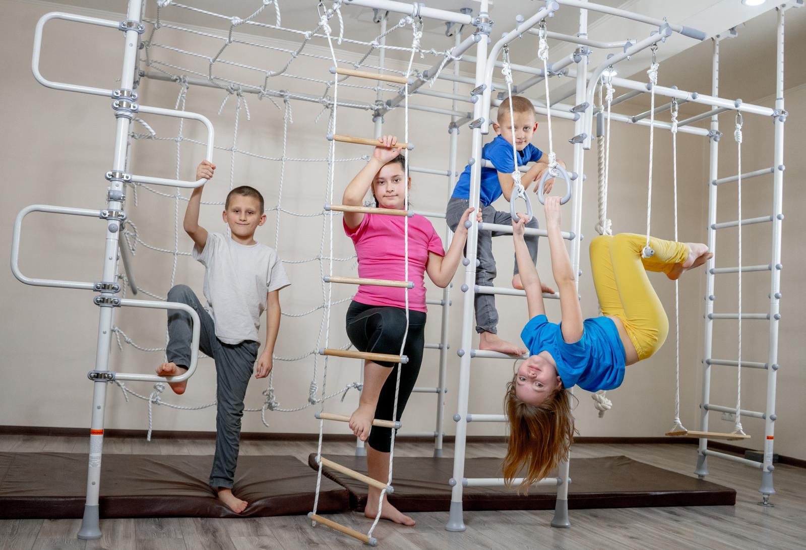 Four children of different ages climbing, hanging, and swinging together on one Brainrich modular play gym
