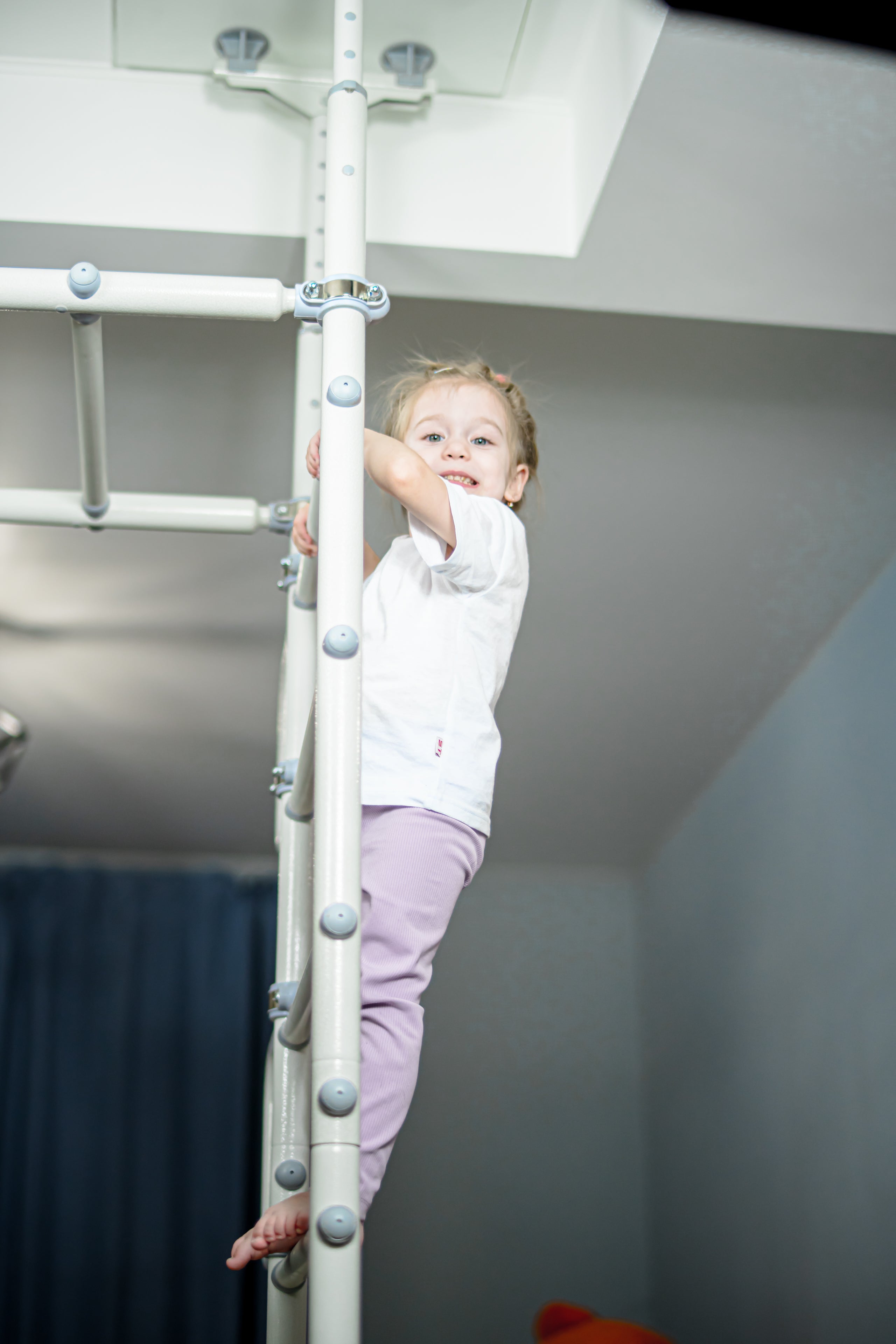 Young girl climbing the ladder of a Brainrich indoor play gym at home, the kind of PE equipment some ESA programs cover