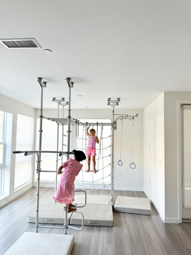 Two kids exercising on a Brainrich indoor home gym, climbing the net and balancing on the trapeze