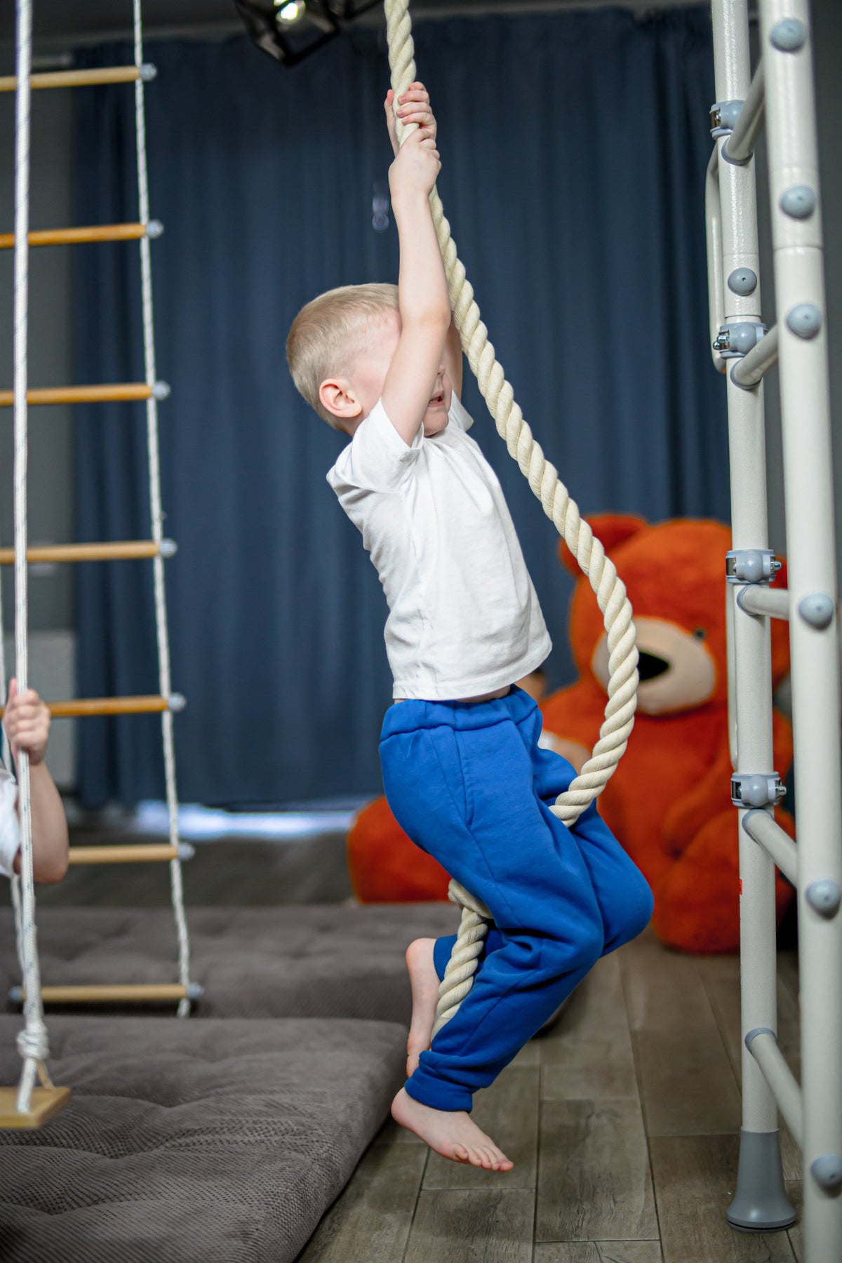 Boy climbing the rope on an indoor play gym in a family playroom