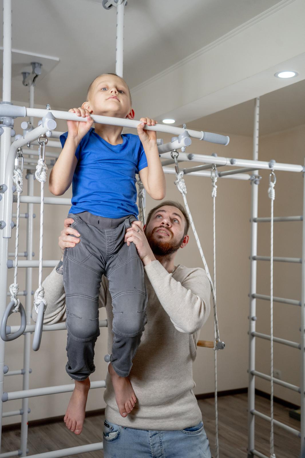 Dad lifting his son to the overhead bar of a Brainrich Mega Max indoor gym