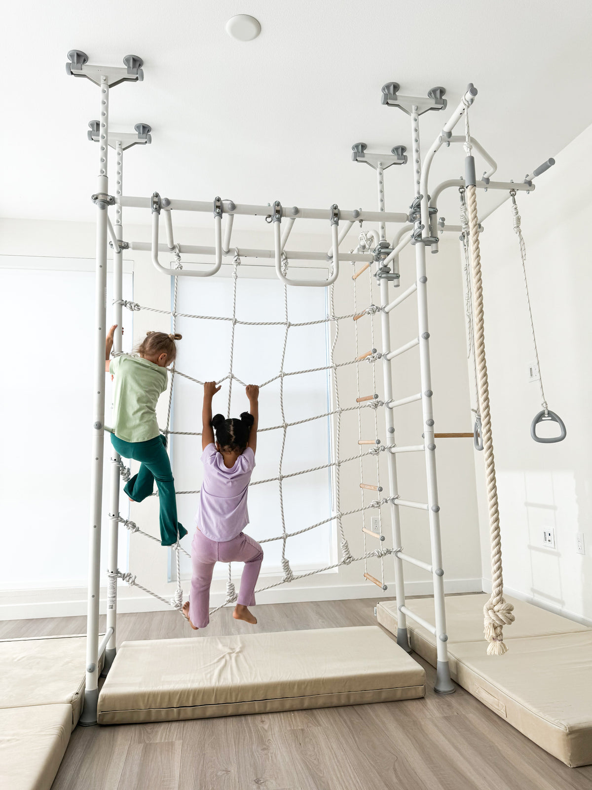 Two girls on the climbing net beneath the monkey bars of a Brainrich Spider gym