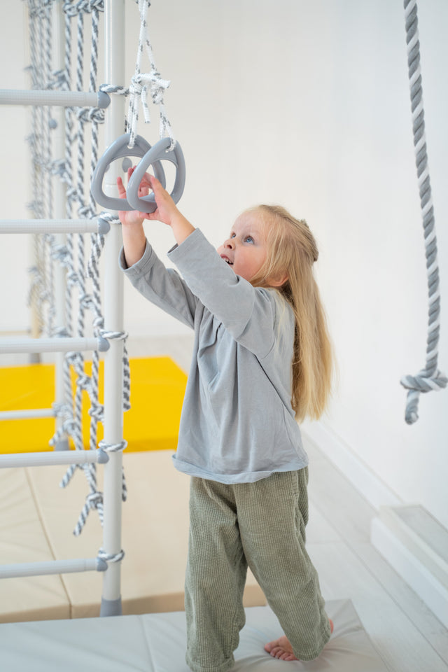 Toddler reaching for gymnastic rings on a Brainrich play gym with a parent nearby
