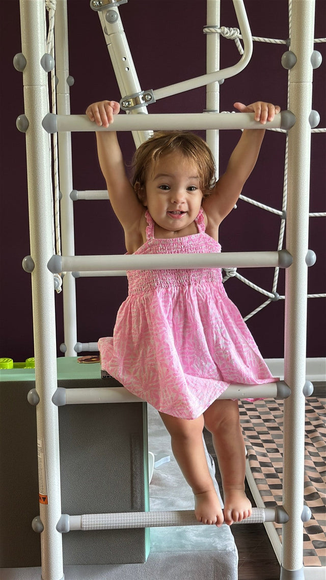 Smiling toddler girl holding the low rungs of a Brainrich indoor play gym ladder at home