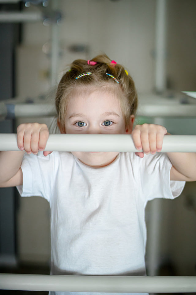 Toddler girl peeking over the bar of a Brainrich indoor play gym