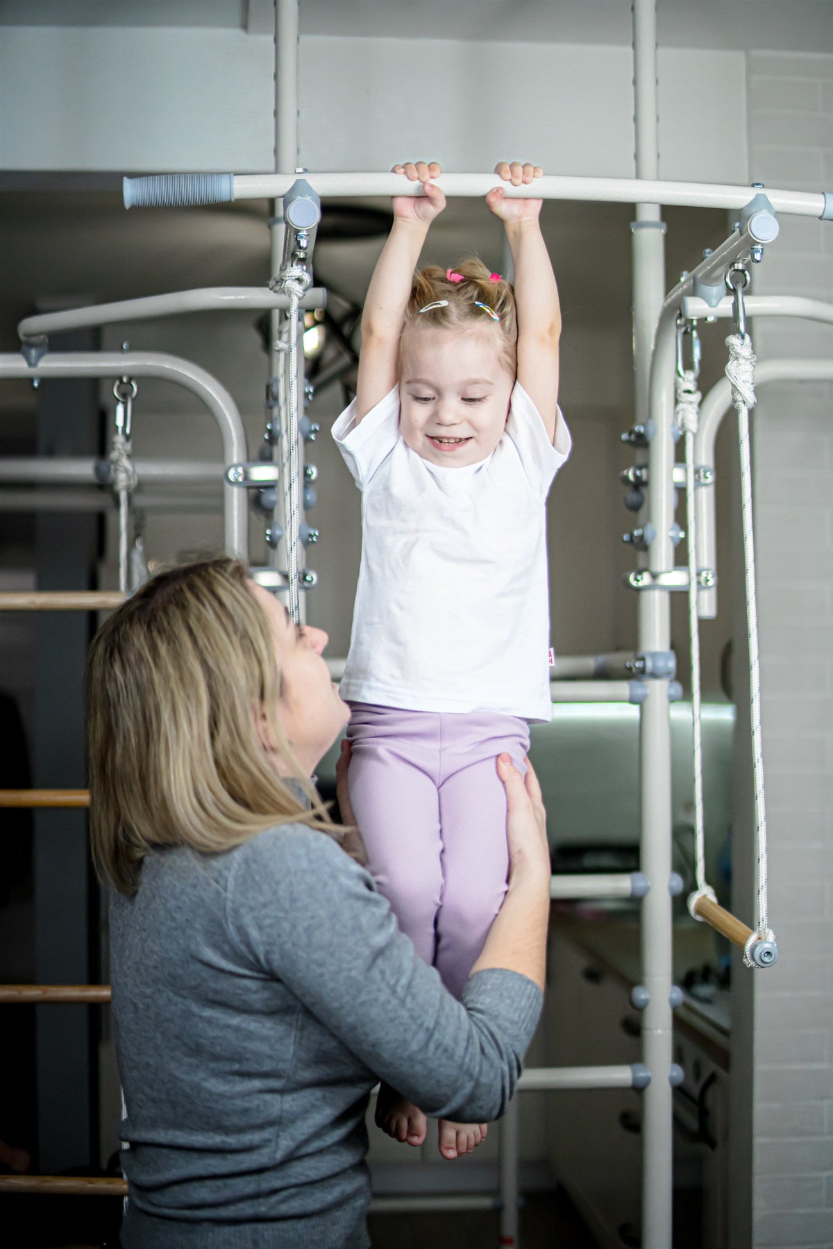 Mom lifting her toddler daughter to hang from the bar of a Brainrich steel home play gym