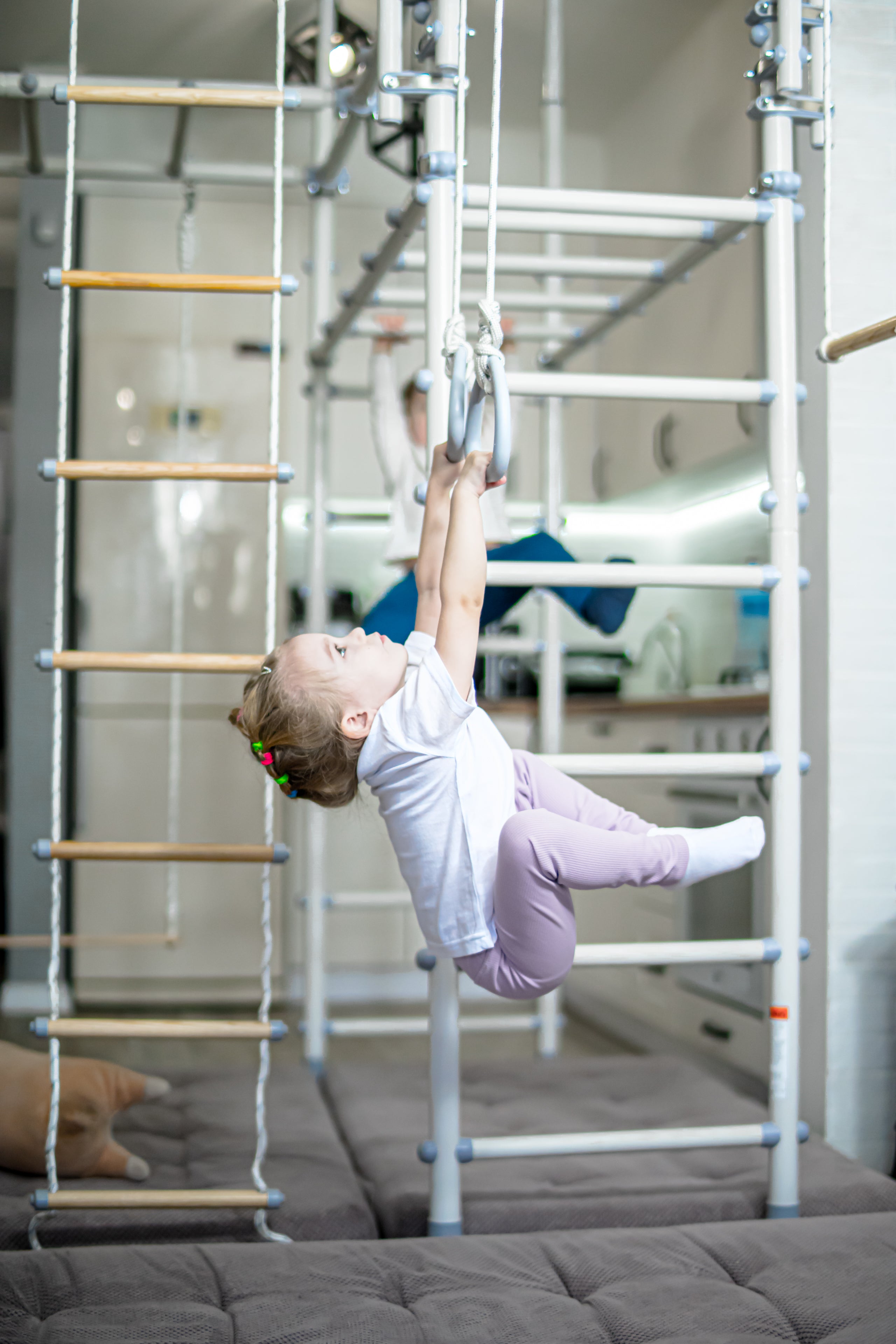 Young girl calmly reaching for gymnastics rings on a Brainrich home play gym, a sensory movement break in an autism homeschool
