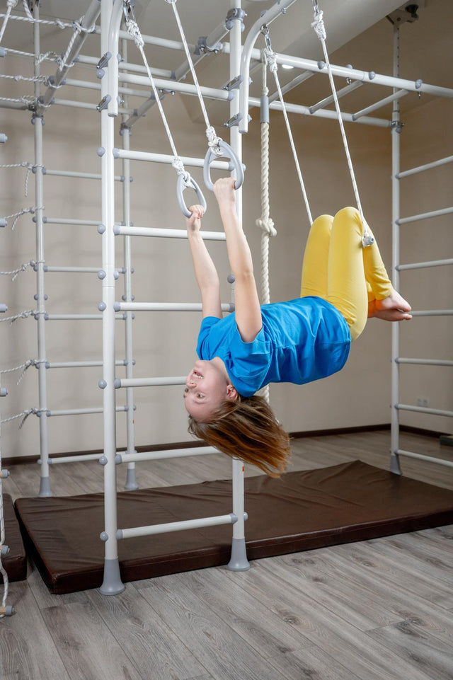Girl hanging upside down from gymnastic rings on a Brainrich home play gym with safety mats below