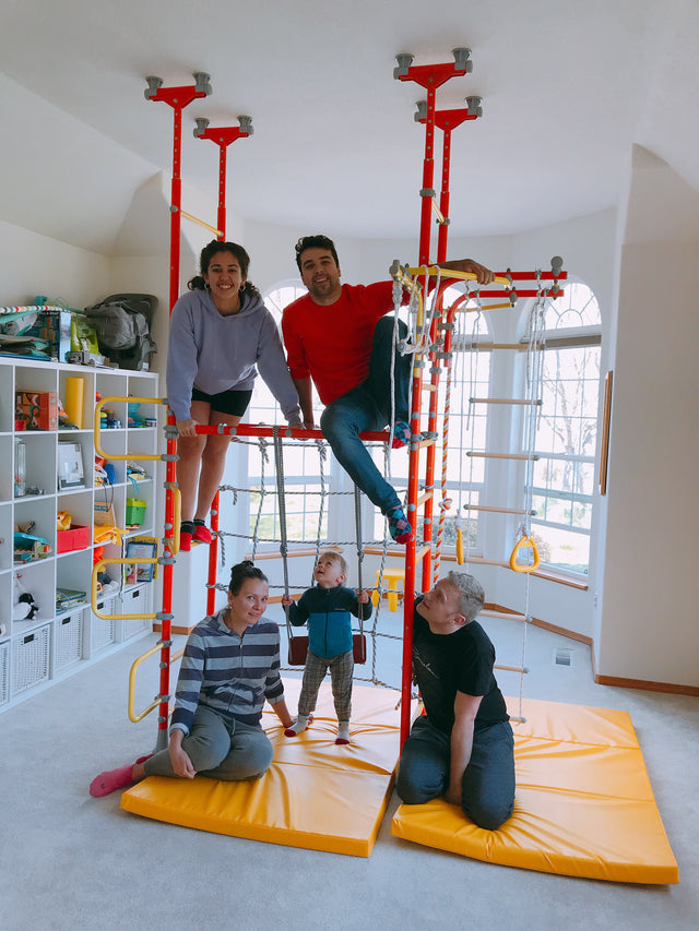 A family in a finished homeschool playroom with a Brainrich play gym, impact mats, and storage shelving