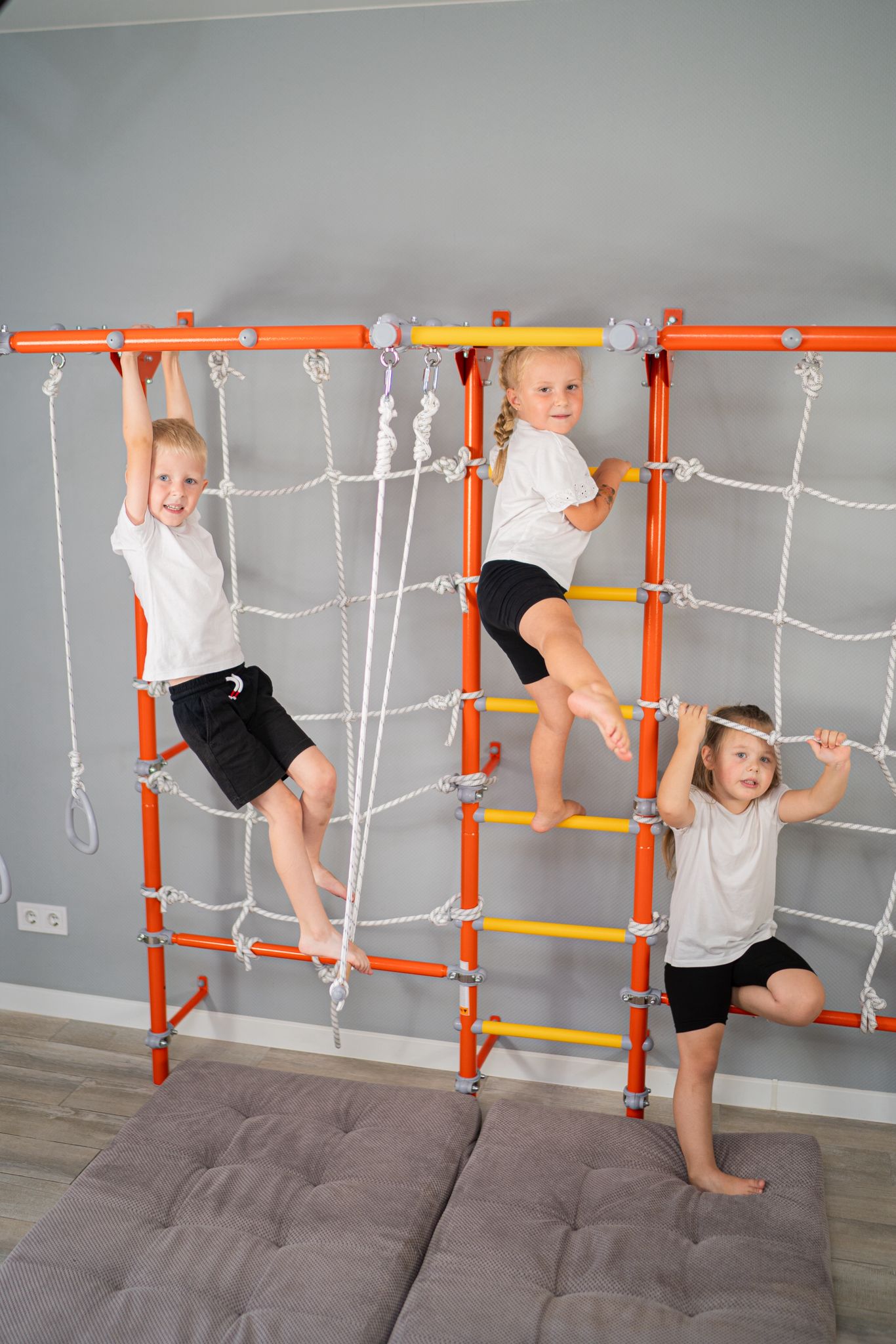 Three kids climbing a wall-mounted Brainrich play gym between lessons, the movement blocks of a homeschool schedule