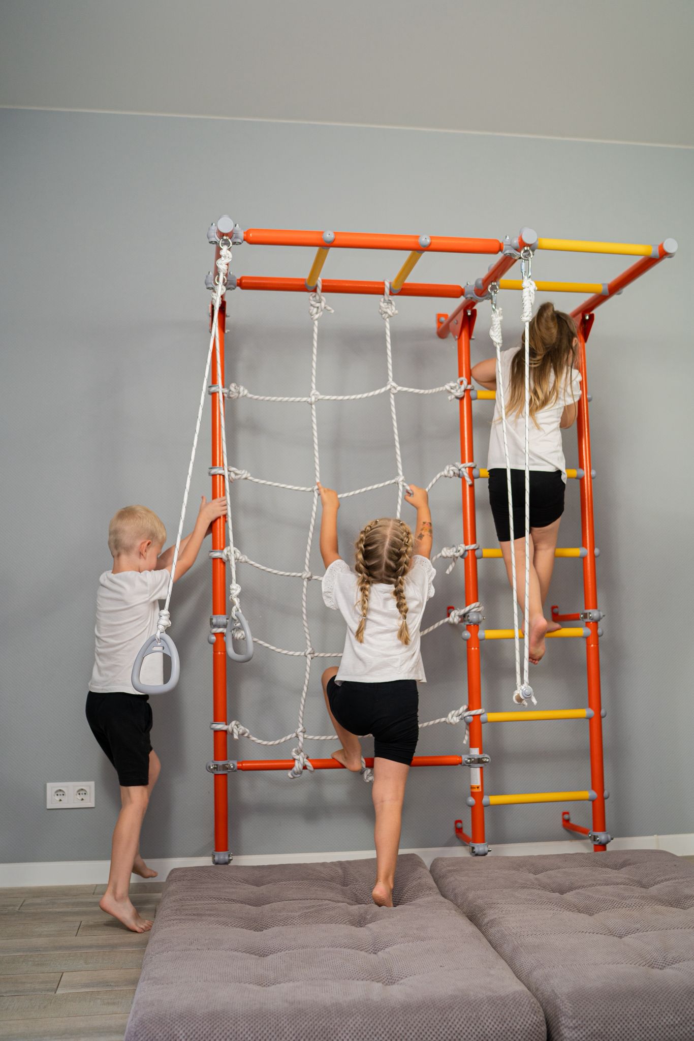Three kids learning through movement, climbing the net and ladders of a wall-mounted Brainrich play gym