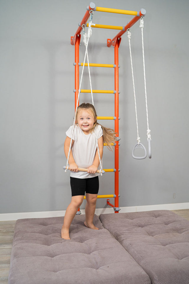 Young girl taking a movement break on a Brainrich wall-mounted play gym, holding the trapeze bar