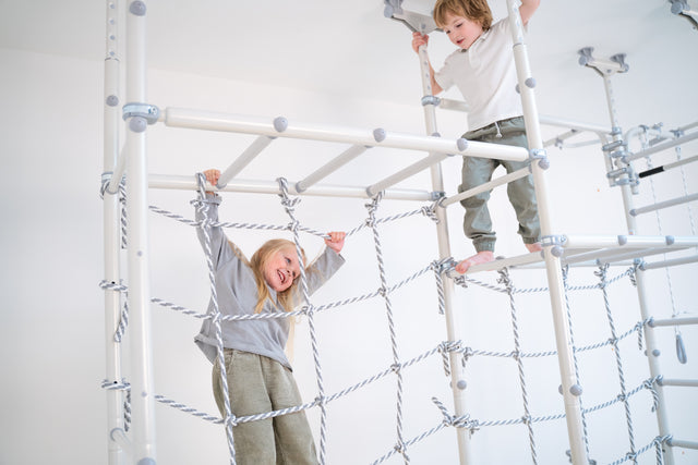 Girl hanging from a climbing net working muscles and joints, deep proprioceptive input on a Brainrich gym