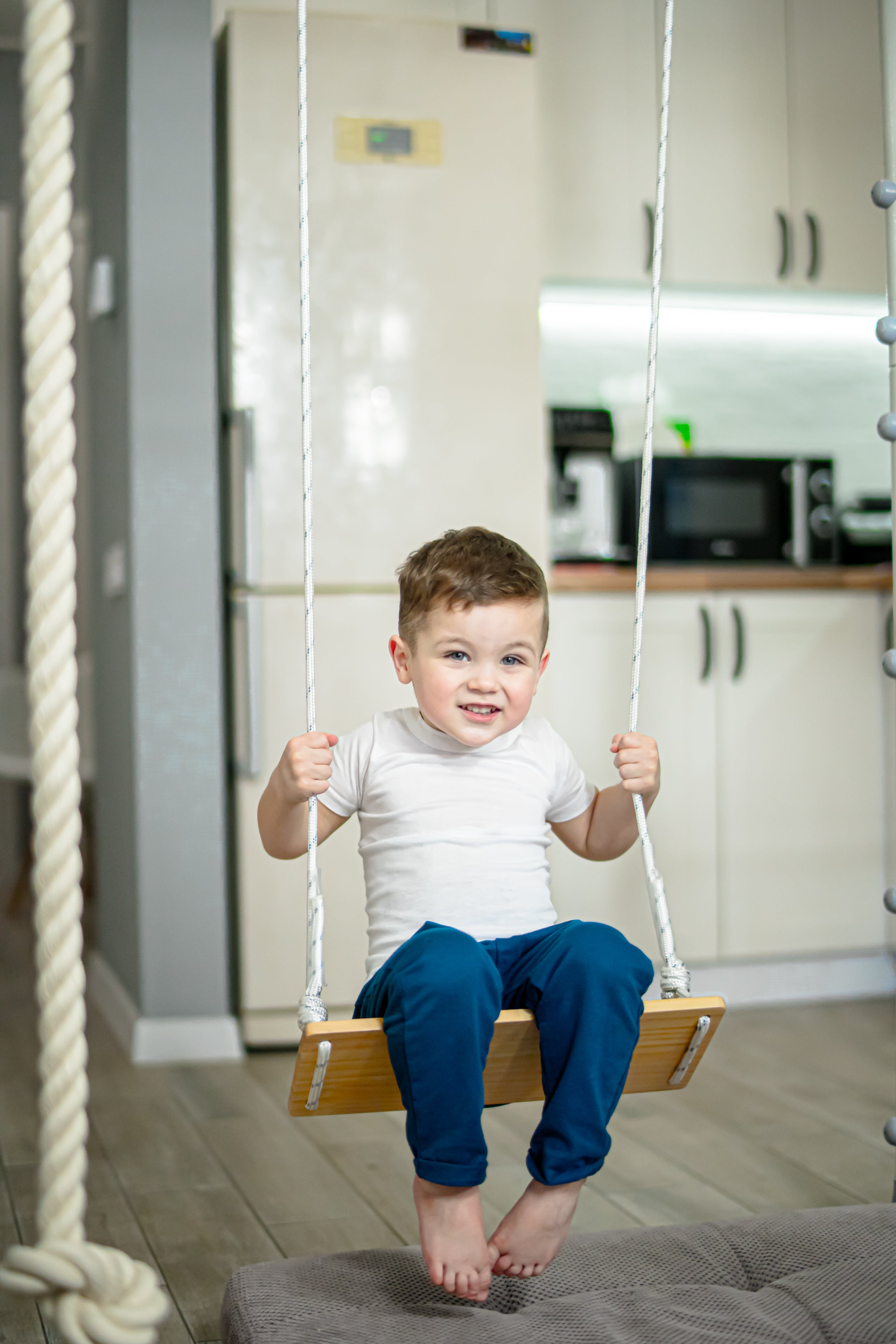 Toddler on a classic wooden sensory swing hanging from a Brainrich play gym frame with a mat below