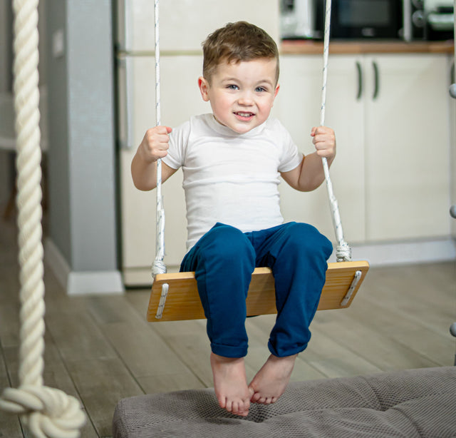Child on an indoor swing hung from a Brainrich steel play gym