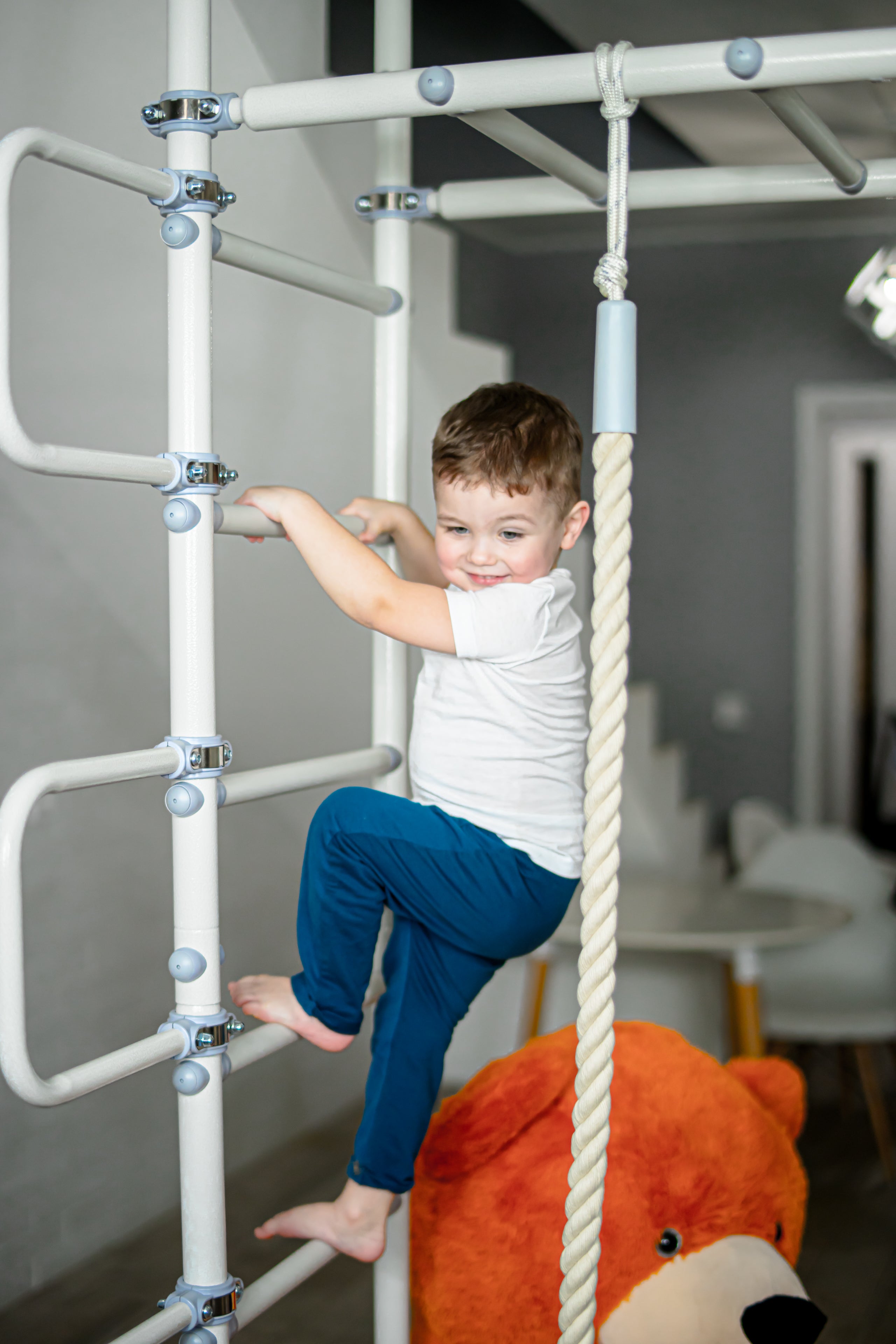 Smiling toddler climbing the ladder rungs of a Brainrich steel indoor play gym at home
