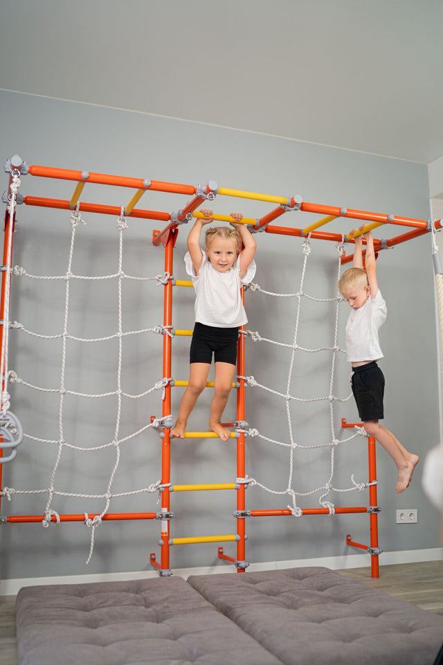 Two kids climbing a wall-mounted Brainrich play gym in a small room, showing a vertical movement zone with almost no floor footprint