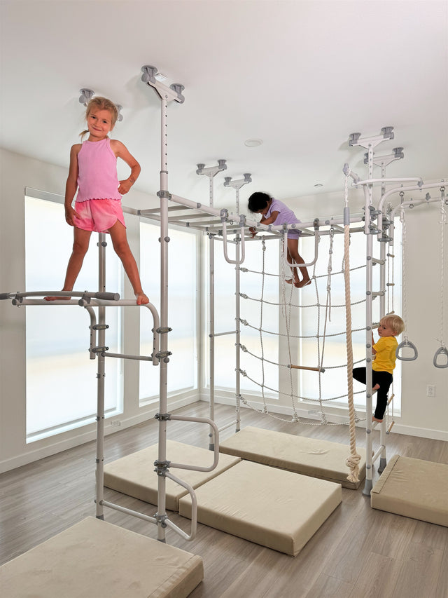 Three kids climbing on a white Brainrich indoor play gym in a bright room, the indoor movement zone that carries a year-round homeschool schedule through every season